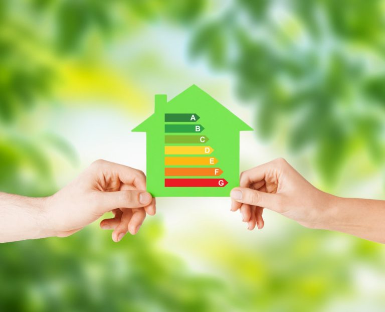 Concept of an energy-efficient home. Two hands holding a green paper with energy-saving ratio over a green background