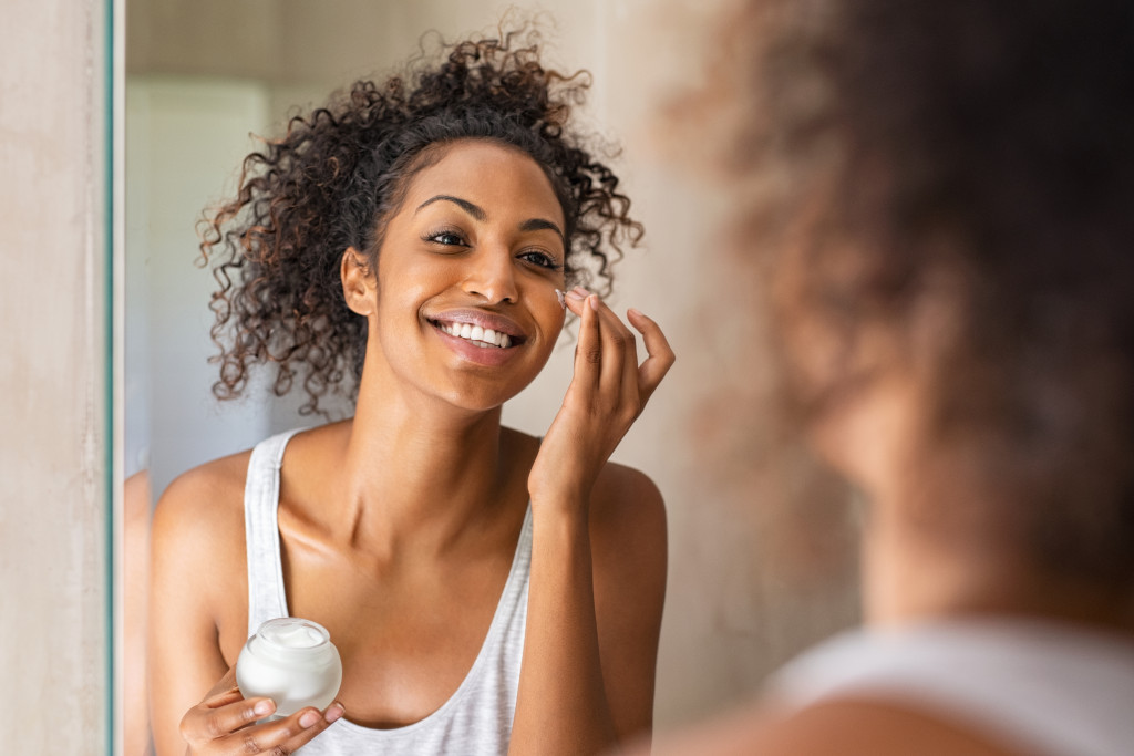 a woman using cream on face infront of the mirror
