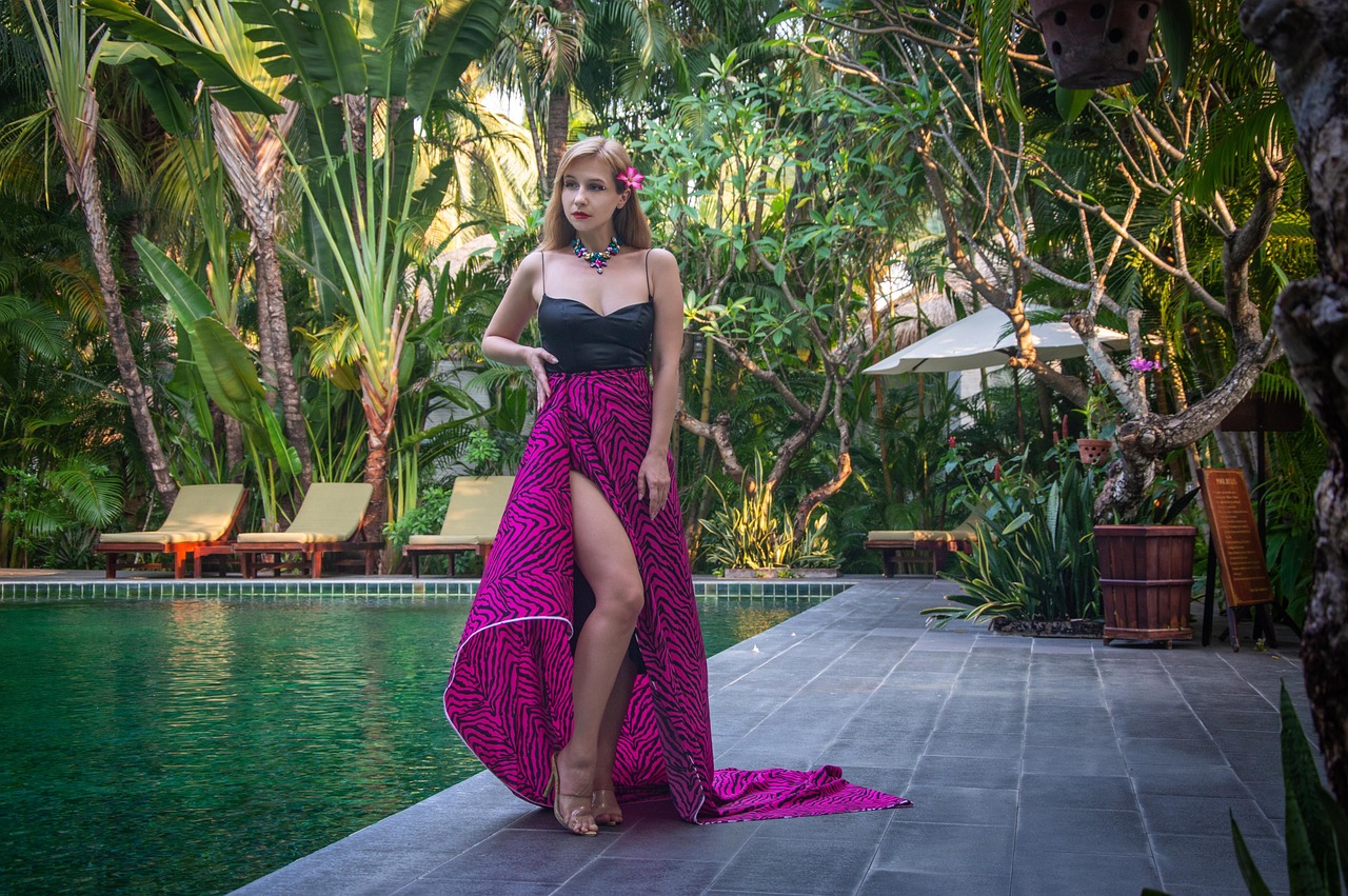 woman wearing a fuchsia pink patterned maxi skirt with a slit and a silk sleeveless top by a swimming pool